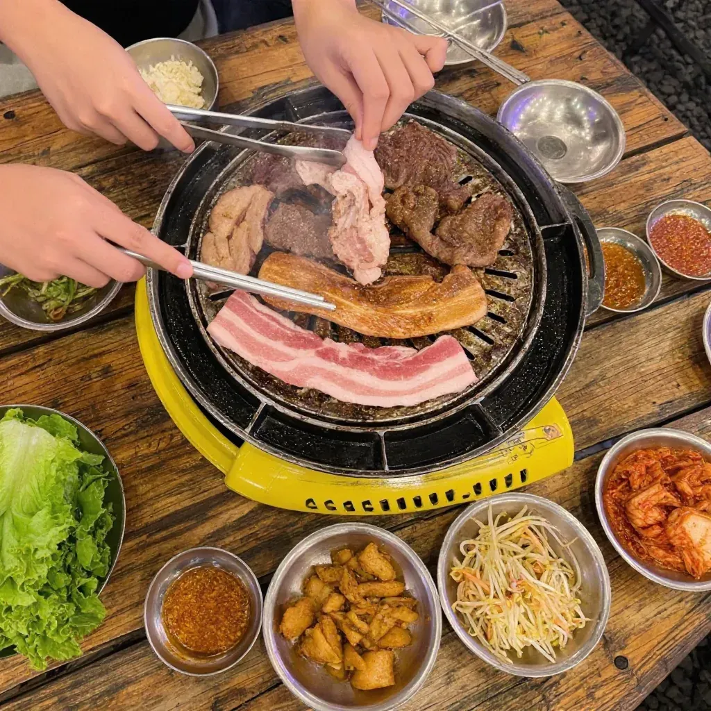 Overhead view of hands grilling meat on a portable SharEat tabletop grill, surrounded by side dishes