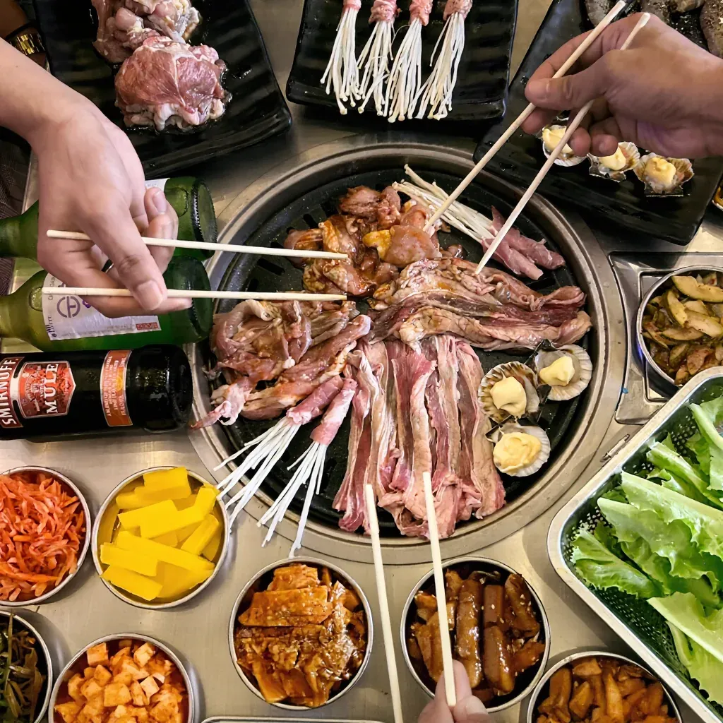 Overhead view of raw meats, lettuce, and side dishes laid out around a SharEat grill, ready to cook